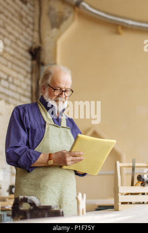 Close-up Seitenansicht schoss der älteren Mann mit Übung Buch in seinem Arbeitszimmer Stockfoto