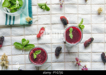 Blick von oben auf die Mulberry mulberry Saft und Obst, frische Beeren Obst und Beeren Smoothies mit Minze auf weißem Stoff. Stockfoto