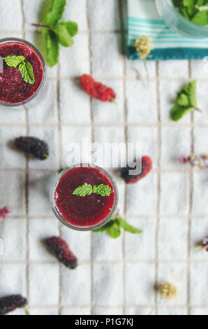 Blick von oben auf die Mulberry mulberry Saft und Obst, frische Beeren Obst und Beeren Smoothies mit Minze auf weißem Stoff. Stockfoto