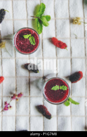 Blick von oben auf die Mulberry mulberry Saft und Obst, frische Beeren Obst und Beeren Smoothies mit Minze auf weißem Stoff. Stockfoto