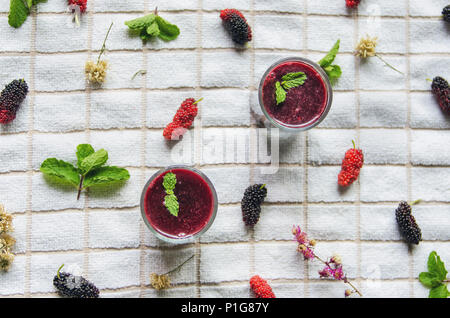 Blick von oben auf die Mulberry mulberry Saft und Obst, frische Beeren Obst und Beeren Smoothies mit Minze auf weißem Stoff. Stockfoto