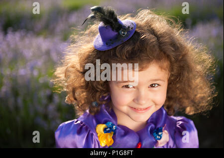 Portrait von glücklich schöne kleine Mädchen in Hütchen und lila Kleid unter den Blumen Stockfoto