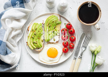 Frühstück avocado Toast mit Spiegelei, Tomaten, Tasse Kaffee und weißen Blüten. Frühstück im Bett. Gesunde Lebensweise, gesunde Ernährung Konzept Stockfoto