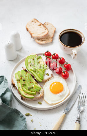 Toast mit Avocado, Spiegelei, Tomaten und Kaffee. Gesundes Frühstück auf Weiß konkreten Hintergrund. Selektive konzentrieren. Gesunder Lebensstil Konzept Stockfoto
