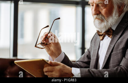 Alter Mann mit schlechtem Sehvermögen, die versuchen, ein Bild auf dem Bildschirm des Tablet auskundschaften Stockfoto