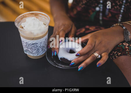 Nahaufnahme der Hände der schwarzen Frau mit Kaffee und Donut und schöne Maniküre Stockfoto