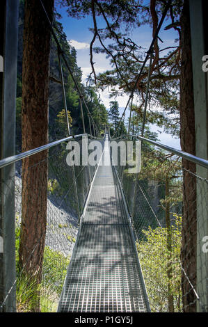 Suspension Bridge Fahren von steilen Felswänden in den Schweizer Alpen, Wallis, Schweiz. Fußgängerweg durch Baumkronen. Grüne Landschaft, blauen Himmel. Stockfoto