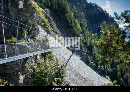 Suspension Bridge Fahren von steilen Felswänden in den Schweizer Alpen, Wallis, Schweiz. Fußgängerweg durch Baumkronen. Grüne Landschaft, blauen Himmel. Stockfoto