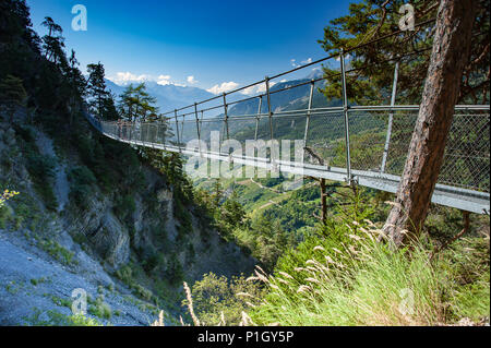 Suspension Bridge Fahren von steilen Felswänden in den Schweizer Alpen, Wallis, Schweiz. Fußgängerweg durch Baumkronen. Grüne Landschaft, blauen Himmel. Stockfoto