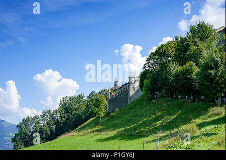 Blick auf die Stadtmauern und Tor von Gruyeres, Altstadt der Schweiz. Wunderschöne grüne Landschaft, Baum überstiegen Hang und blauen bewölkten Himmel Stockfoto