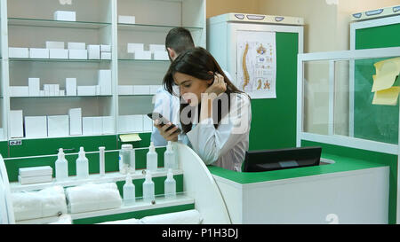 Junger Apotheker broqsing per Handy am Arbeitsplatz Langweilen Stockfoto