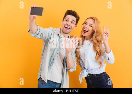 Portrait von Mann und Frau Berücksichtigung selfie Foto auf Handy gestikulierend an der Kamera mit den Fingern über Gelb Hintergrund isoliert Stockfoto