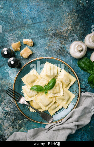 Platte von Ravioli mit Pilzen und Käse von Basil auf dunklem Stein dekoriert, Ansicht von oben Stockfoto