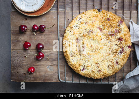 Hausgemachten Kirschkuchen mit frischen Beeren auf rustikalen Hintergrund bröckeln, Ansicht von oben Stockfoto
