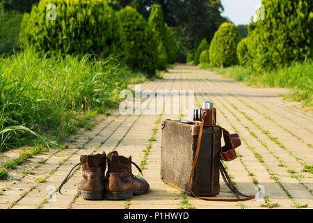 Mit leichtem Gepäck reisen! Schäbig Ankle Boots neben einem vintage Karton Koffer, ein Film Kamera in seine offene Ledertasche und ein yellow brick road. Stockfoto