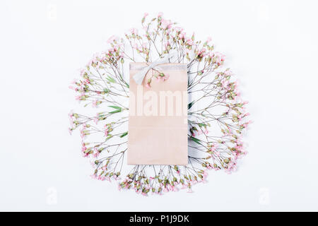 Runden Rahmen der rosa Blüten mit einem Geschenk Beutel in der Mitte, oben sehen. Flache florale Gestaltung von festlichem Dekor auf weißem Hintergrund. Stockfoto