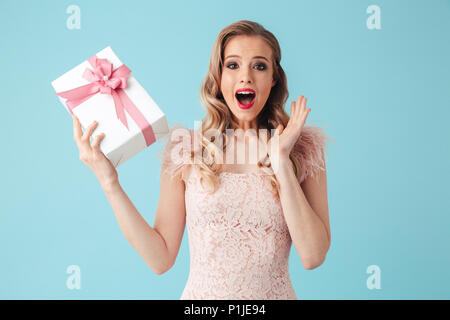 Gerne blonde Frau in Kleid holding Geschenkkarton überrascht, und wenn man die Kamera über Türkis Hintergrund Stockfoto