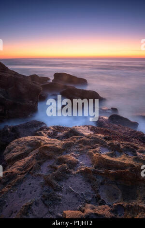 Felsen und Wellen in der langzeitbelichtung bei Sonnenuntergang am Atlantik, Praia Santa Cruz, Portugal Stockfoto