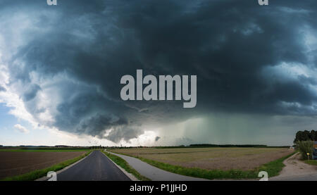 Panoramablick auf das Bild einer Superzelle mit wall cloud, gut definierten Aufwind eine grün leuchtende Niederschlag Kern einer klassische Superzelle über eine Straße in der Nähe von Heilsbronn, Bayern, Deutschland Stockfoto