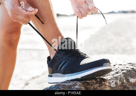 Nahaufnahme von einem Mann binden binden Schuhbändern auf seinen Turnschuhen im Freien an der Küste Stockfoto