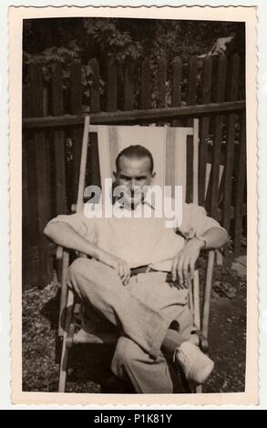 DIE TSCHECHOSLOWAKISCHE SOZIALISTISCHE REPUBLIK - UM 1950s: Ein Vintage-Foto zeigt, wie der Mensch auf einem Holz-/Textildeckstuhl im Garten sitzt. Schwarzweiß-Fotografie. 1950s Stockfoto