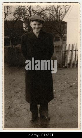 DIE TSCHECHOSLOWAKISCHE SOZIALISTISCHE REPUBLIK - UM 1950s: Ein Vintage-Foto zeigt, wie ein junger Mann mit Spitzenmütze im Freien posiert. Holzzaun und Haus ist im Hintergrund. Schwarzweiß-Fotografie.1950s Stockfoto