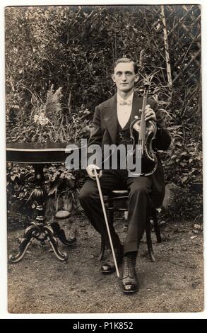 DIE TSCHECHOSLOWAKISCHE REPUBLIK. - UM 1930s: Vintage-Foto zeigt jungen Mann posiert mit der Geige im Freien. Der Geiger sitzt am schwarzen eleganten Tisch. Antike Schwarz-Weiß-Fotografie. 1930s. Stockfoto