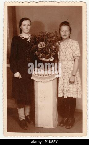 DEUTSCHLAND - UM 1930s: Auf einem Vintage-Foto posieren Frauen im Fotostudio mit Blumenstrauß auf einem weißen Podest. Schwarze & weiße antike Fotografie. 1930s Stockfoto