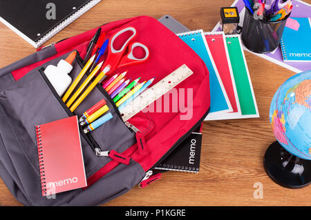 Rucksack mit einem Sortiment von Schulmaterial auf einem Desktop - Zurück zu Schule Konzept Stockfoto