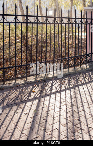 Metallzaun und ihren Schatten auf Bürgersteig auf sonnigen Herbsttag. Stockfoto