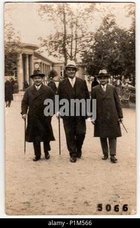 LAZNE PODEBRADY, DIE TSCHECHOSLOWAKISCHE SOZIALISTISCHE REPUBLIK - UM 1950s: Ein Vintage-Foto zeigt, wie drei Männer im Kurort spazieren gehen. Kolonnade im Hintergrund. Stockfoto