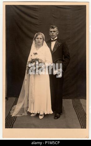 Die tschechoslowakische Republik - circa 1930s: Vintage Foto der Jungvermählten. Die Braut trägt einen langen Schleier und hält Wedding Bouquet. Der Bräutigam trägt schwarzen Anzug und Fliege. Schwarz & Weiß antik Studio Portrait. Stockfoto