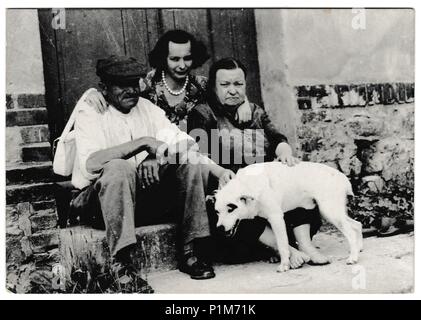 Die tschechoslowakische SOZIALISTISCHE REPUBLIK - ca. 1960er-Jahre: Retro Foto zeigt die ländliche Bevölkerung auf einer Türschwelle mit Hund sitzen. Schwarz & Weiß vintage Fotografie Stockfoto