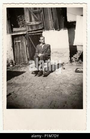 Die tschechoslowakische Republik - September 20, 1942: Retro Foto zeigt einen jungen Mann auf dem Schaukelstuhl im Hinterhof befindet. Vintage Schwarz/Weiß-Fotografie. Stockfoto