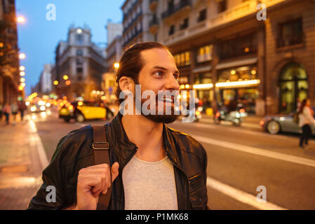 Portrait von lächelnden europäischen Mann mit gebunden Haar zur Seite schauen, während man durch Megapolis in Abend Stockfoto