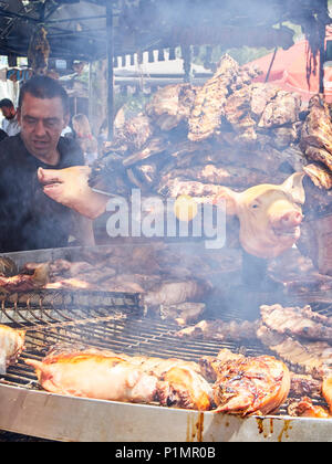 Hispanic Koch, Schweinerippchen und andere Fleischsorten Schnitte auf Holzkohle Grill in einem Stall eines Street Food Fair. Stockfoto