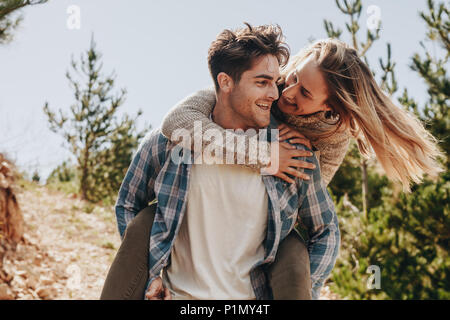 Hübscher junger Mann, der piggyback Ride zu seiner Freundin. Paar Spaß im Freien auf einem Berg Trail. Stockfoto