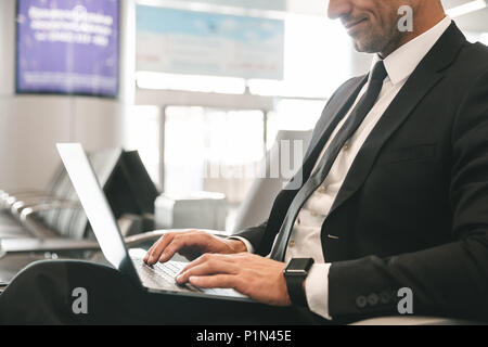 Zugeschnittenes Bild der Geschäftsmann in Anzug gekleidet mit Laptop Computer während am Flughafen Lobby sitzen Stockfoto