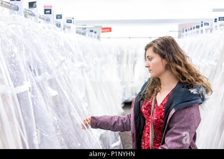 Junge Frau auf der Suche versuchen auf berühren Hochzeit Kleid in Boutique Discounter, viele weiße Kleider hängen an Rack Kleiderbügel Zeile Stockfoto