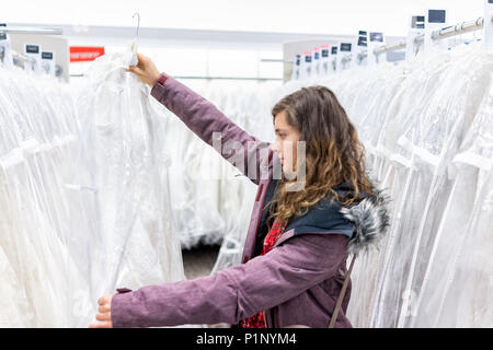 Glückliche junge Frau mit einem lace Wedding Dress in Boutique Discounter, viele weiße Kleider hängen an Rack Kleiderbügel Zeile Stockfoto