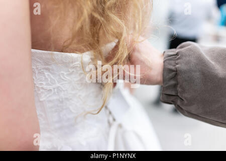 Nahaufnahme zurück der jungen Frau und Mutter, die versuchen, auf geschnürten Korsett Hochzeit Kleid in Boutique Discounter mit Schnürung Ribbon, blondes Haar Stockfoto