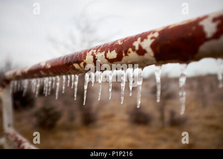 Eiszapfen hängen von einem alten rostigen ländlichen Pole auf einem Hof oder Zaun an einem Wintermorgen in eisigen Wetter Stockfoto