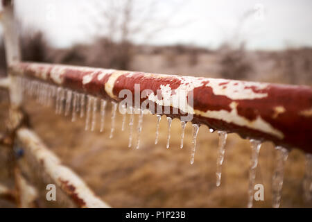 Altes rostiges Metall bar in Eis mit unten Eiszapfen hängen auf einem Hof oder Zaun im Winter Wetter überdacht Stockfoto