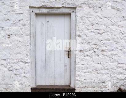 Alte Weiße verwitterten hölzernen Tür auf einem weiß getünchten Gebäude aus Stein Stockfoto