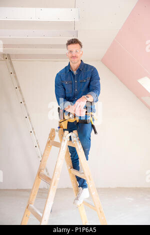 Volle Länge von Stattlichen im mittleren Alter Heimwerker stehen auf der Leiter auf der Baustelle. Stockfoto