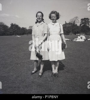 1947, nach dem Zweiten Weltkrieg Großbritannien und zwei junge Senior School Mädchen tragen ihre einheitliche, kurze Socken, stehen zusammen in einem Park, der nach der Schule, England, UK. Stockfoto