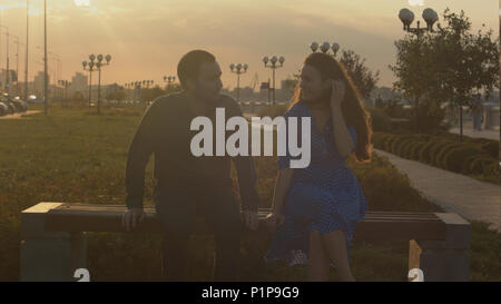 Mann und Frau sprechen, sitzt auf der Bank während des Sonnenuntergangs. Stockfoto