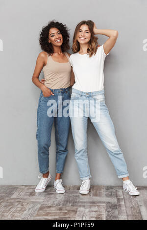 In voller Länge Porträt von zwei lächelnde junge Frauen zusammen über grauer Hintergrund stehen isoliert Stockfoto