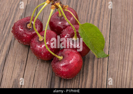 Bündel gewaschen Süßkirschen auf Holz Hintergrund. Prunus avium. Schönen frischen roten Beeren. Gesundes Steinobst, grünes Blatt, Wasser tropfen. Stockfoto