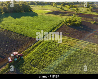 Luftbild von der Drohne, einen Blick aus der Vogelperspektive auf landwirtschaftlichen Feldern mit einer Straße durch und einem Traktor und Auto im Frühjahr Abend bei Sonnenuntergang Stockfoto